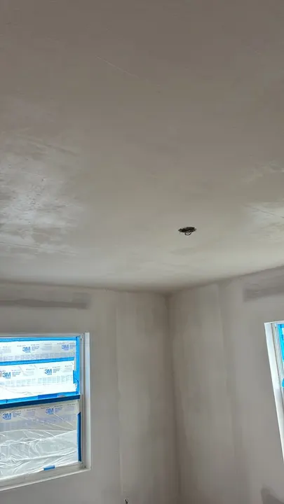 Bedroom ceiling and walls after a skim coat, windows masked for spraying